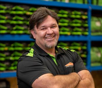 Ryan is a white male with black hair and a beard. He is wearing a black and green servpro polo