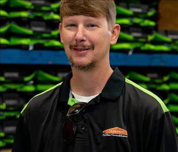 Chris is a white male with brown hair and goatee wearing a black and green servpro polo