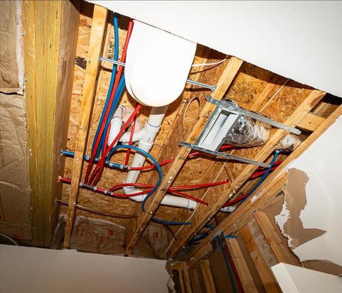 Ceiling with exposed wooden beams, insulation, and pipes, showcasing plumbing and electrical work in progress, featuring PEX 